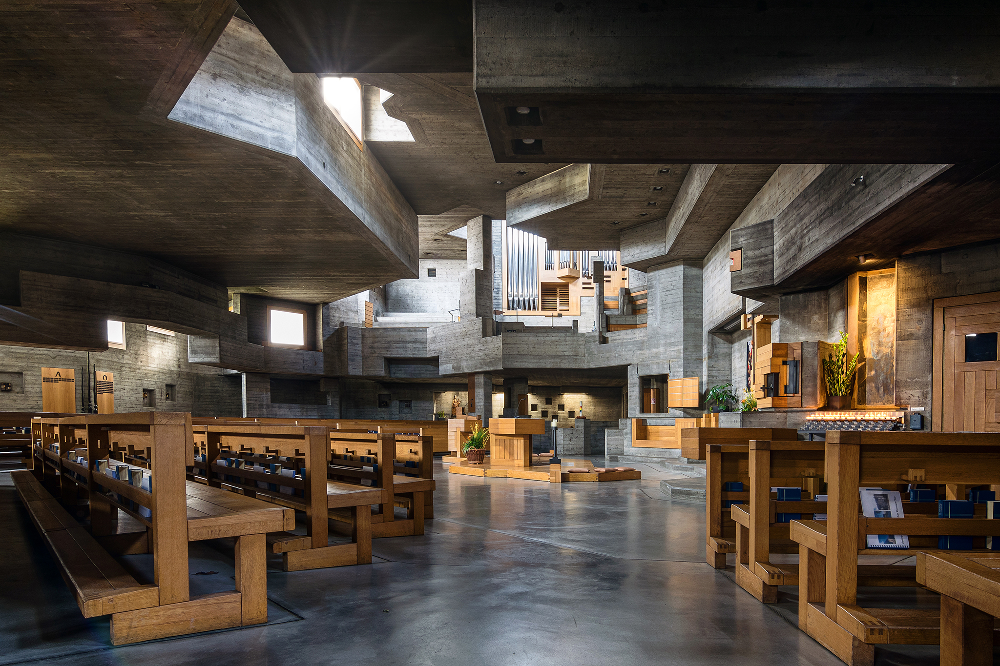 Eine Kirche mit Holzbänken und einer Decke aus Beton, die eine ruhige und moderne Atmosphäre ausstrahlt.